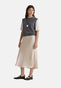 Suéter de punto gris de manga corta sobre un vestido midi fluido de color crema, combinado con bailarinas negras con correas ajustables.