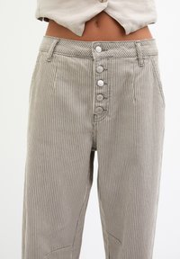 Striped lightweight trousers in beige and white, featuring a high waist, six button front closure, and two side pockets.