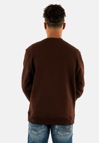 Bruine sweatshirt met een ronde hals en geribde manchetten. Gemaakt van zacht materiaal, heeft een eenvoudige uitstraling met een gestikt detail aan de achterkant.