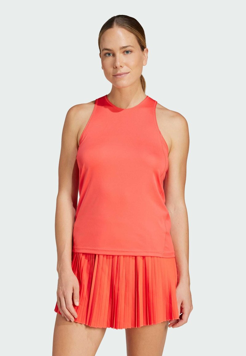 Débardeur de sport corail avec un col montant et une coupe sans manches, associé à une jupe plissée corail, mettant en valeur un tissu lisse et une couleur éclatante.