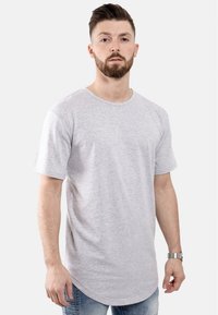 Graues Kurzarm-T-Shirt mit rundem Halsausschnitt, aus weichem Stoff gefertigt. Mit abgerundetem Saum und lockerer Passform. Getragen mit blauen Jeans.