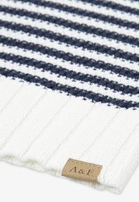 Megztas kepurė su baltais ir tamsiai mėlynais horizontaliais dryžiais, išsiskirianti raukšlėtu tekstūra ir ruduo odiniu ženklu su "A&F" emblema.