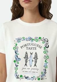 Witte katoenen T-shirt met een ontwerp met blauwe en groene bloemaccenten, zwart en blauwe visafbeeldingen, en tekst: "PORTUGESE SMAAK."