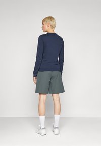 Jūrinis ilgo rankovės megztinis, derinamas su pilkais šortais. Modelis dėvi baltas kojines ir šviesiai pilkas sportines batus. Paprastas dizainas, kasdienis siluetas.