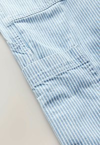Tissu rayé bleu et blanc avec une texture lisse, présentant un poignet replié et un surjet soigné sur le bord.