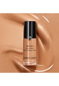 Giorgio Armani Fluid Sheer glow enhancer in een doorzichtig flesje met een zwarte dop. Goudkleurige vloeistof op een gladde, glinsterende gouden achtergrond.