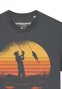 Grijze T-shirt met een zonsondergangontwerp waarop een silhouet van een visser te zien is die een vis vangt, afgezet tegen oranje en gele gradient strepen.
