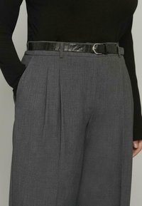 Szare, dopasowane spodnie z plisami, z czarnym paskiem z tłoczeniem w stylu krokodylej skóry i srebrną klamrą, wykonane z gładkiej, teksturowanej tkaniny.