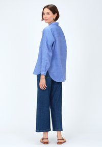 Camicia in lino azzurro chiaro con una vestibilità rilassata, colletto e maniche arrotolate, abbinata a pantaloni in denim larghi e scuri e sandali beige.