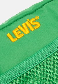 Zielony materiał z teksturowanym, siatkowym fragmentem. Posiada haftowane logo "Levi's" w kolorze pomarańczowym, wyraźnie widoczne na powierzchni.