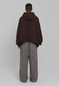 Sweat à capuche marron surdimensionné avec une coupe décontractée et des poignets côtelés, associé à un pantalon cargo gris ample avec poches arrière.