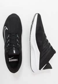 Zwarte hardloopschoenen met een bovenwerk van mesh, een gevoerde zool, het kenmerkende Nike-logo en een witte buitenzool voor grip. Accenten omvatten geweven panelen.