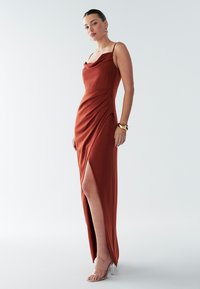 Klänningskväll i rostfärgad färg av silkesliknande tyg med draperad halsringning, sidosprund och plisserad detalj. Har tunna band och en kroppsnära silhuett.