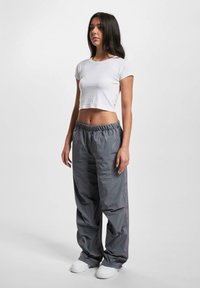 Pantaloni grigi leggeri e larghi con una vita elasticizzata, abbinati a un crop top bianco aderente. Tessuto liscio e design casual.