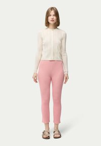 Ribbad krämfärgad stickad tröja med långa ärmar och framknäppning, matchad med högmidjade rosa ribbade leggings, fulländad med platta sandaler.