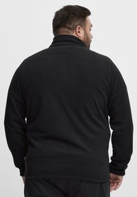 Pullover in pile nero con colletto alto, texture morbida e maniche lunghe. Presenta un orlo dritto e una vestibilità rilassata, vista da dietro.