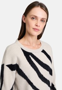 Gebreide trui in lichtbeige met gedurfde zwarte abstracte strepen. Voorzien van een ronde halslijn en een zachte, gestructureerde stof.