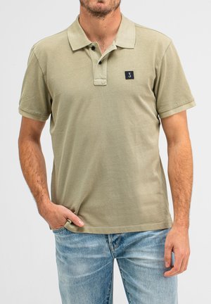 Olivgrünes Poloshirt aus strukturiertem Baumwollstoff, mit einer Knopfleiste mit drei Knöpfen, kurzen Ärmeln und einem kleinen schwarzen Logo-Patch auf der Brust.