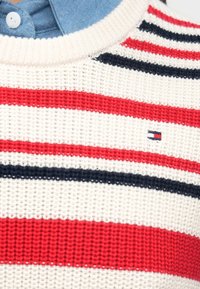 Ριγέ πλεκτό πουλόβερ σε εκρού, κόκκινο και ναυτικό μπλε. Διαθέτει στρογγυλή λαιμόκοψη και μικρή λεπτομέρεια με λογότυπο στο στήθος. Υφή με αεριζόμενο ύφασμα.