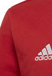 Felpa rossa realizzata in tessuto testurizzato, con logo Adidas ricamato in bianco e scollatura rotonda.