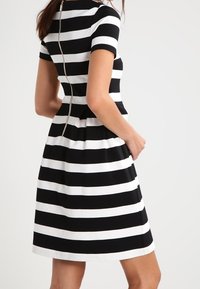 Czarna i biała sukienka w paski z krótkimi rękawami, dopasowaną górą i rozkloszowanym dołem. Posiada widoczny zamek z tyłu. Gładka tekstura materiału.