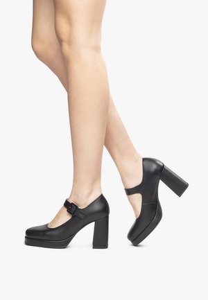 Black leather platform heels with a round toe, a wide block heel, and an ankle strap featuring a rectangular buckle. Smooth texture.
