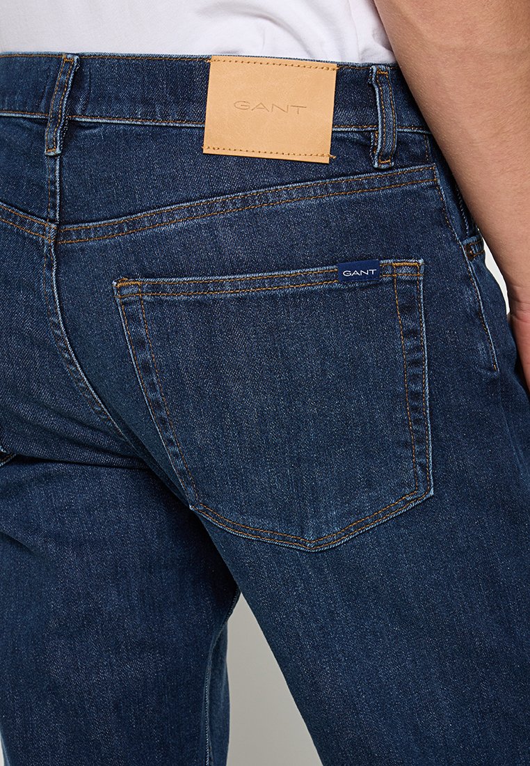 Granatowe dżinsy z ciemnego denimu z skórzaną naszywką logo GANT na pasie, z detalicznym przeszyciem i dwiema tylnymi kieszeniami.