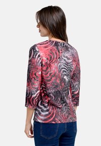 Langärmlige Bluse in verschiedenen Farben in Rottönen, Grau und Schwarz, mit einem wirbelnden Blumenmuster und einem runden Ausschnitt.