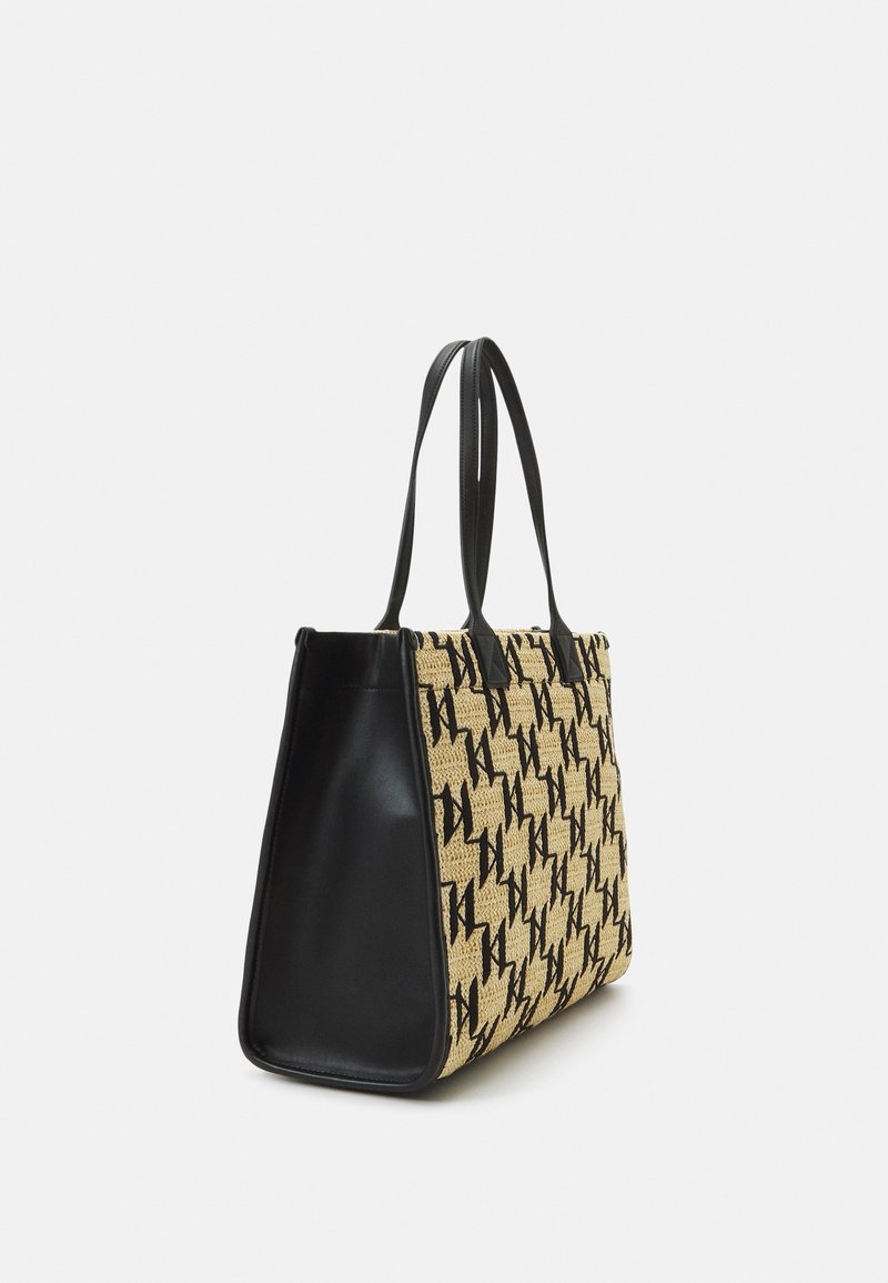Sac fourre-tout avec côtés et poignées en cuir noir, présentant un tissu beige avec un motif monogramme noir répété sur les panneaux avant et arrière.