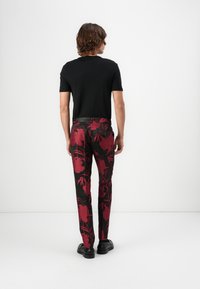 Schwarzes T-Shirt mit kurzen Ärmeln, kombiniert mit einer floral gemusterten Hose, die große rote Blumen auf schwarzem Hintergrund zeigt, und schwarzem Schuhwerk.