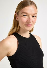 Sort ribbet tanktop med høj hals og ærmeløst design. Glat tekstur og slim fit med detaljer ved skulderskæringer.