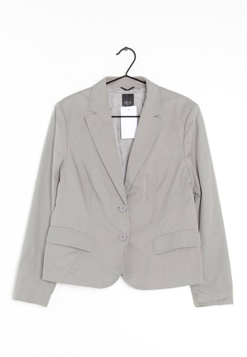 Blazer gris clair avec une coupe ajustée, deux boutons, deux poches avant et des détails de couture visibles. Suspendu à un crochet noir.