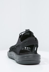 Black sandal with a textured upper, woven detail, adjustable strap, and a rubber sole. Features an open back for ventilation.