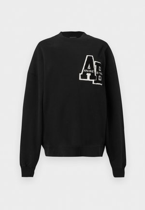 Sweat-shirt noir à col rond avec manches longues et écusson texturé blanc et noir "AD" sur la partie supérieure gauche de la poitrine.