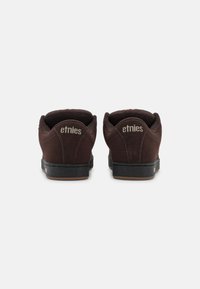 Kohvakoosest suede tossud musta kummitaldaga, mis on varustatud pehmendatud kraega ning kaubamärgi "etnies" nimelaga kontsapadjandil. Lihtne disain.