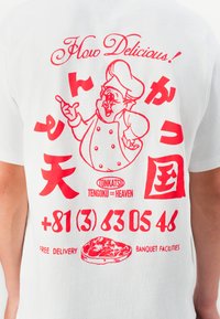 T-shirt blanc avec impression graphique rouge d'un cochon chef, texte japonais, un numéro de téléphone et illustration de viande avec étiquette "Livraison Gratuite".