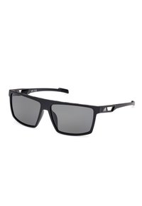 Černé sluneční brýle se čtvercovými skly, šedými tónovanými skly, matným povrchem, texturovanými stranami a výraznými trojúhelníkovými akcenty na rámu.