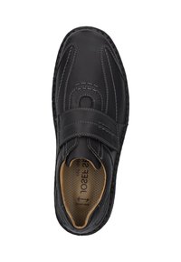 Zapato de cuero negro con punta redonda, correa de velcro, costuras blancas en contraste y una plantilla acolchada marrón. Suela texturizada.
