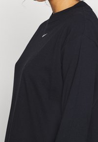 Svart långärmad t-shirt med rund hals och en liten logotyp på bröstet. Tillverkad av mjukt tyg med avslappnad passform och sänkta axelsömmar.