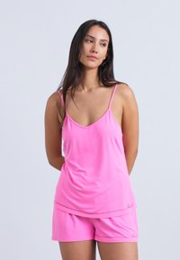 Roosa varrukateta ülikond, mis koosneb siledast kangast särgist ja lühikestest pükstest, mida iseloomustab lõdvestunud lõige ja lühikeste pükste peal peen logo detail.