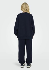 Felpa oversize navy e pantaloni coordinati in jersey di tessuto morbido, con vestibilità ampia, polsini a costine e vita elasticizzata. Sneaker visibili.