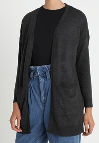 Dark gray knit cardigan with open front, long sleeves, and two front pockets. Worn over a black shirt and high-waisted light blue jeans.