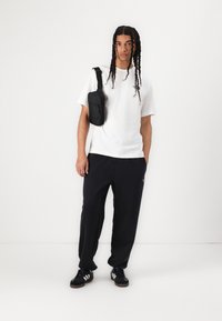 White cotton t-shirt, black drawstring pants, and black sneakers with white stripes. Black crossbody bag hangs from shoulder.