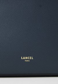 Dark blue textured leather with a pebbled finish; features a gold logo "LANCEL PARIS" at the bottom.
