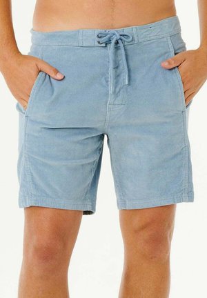 Mand iført lyseblå kordfløjlsshorts med snøre i taljen og hænderne i lommerne mod en hvid baggrund.