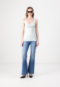 Ljusblå ribbad linne med "GUESS" logotyp, i kombination med ljusblå utsvängda jeans. Svarta högklackade skor. Modell som bär solglasögon.