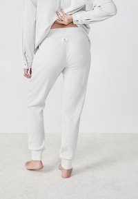 Lichtgrijze geribbelde loungewear set met een losvallende top en taps toelopende broeken. Zachte textuur met elastische manchet en een klein label aan de achterkant.