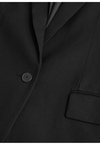 Veste noire sur mesure avec un col à revers cranté, un bouton noir unique, et une poche à rabat sur le côté droit.