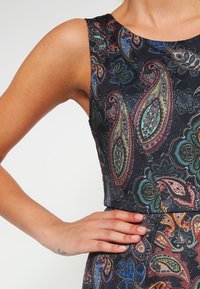 Barevné šaty s paisley vzorem vyrobené z hladké tkaniny; bezrukávový design s přiléhavým korzetem a jemným leskem na tmavém pozadí.