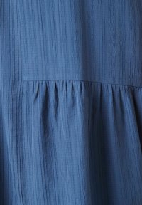 Blaues Kleid aus strukturierten, zerknitterten Stoff. Verfügt über eine geraffte Passe und einen fließenden unteren Bereich, der einen subtilen Layeereffekt erzeugt.